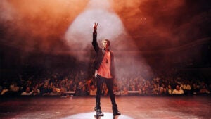 Reza on stage with crowd in background at Reza Edge of Illusion Show